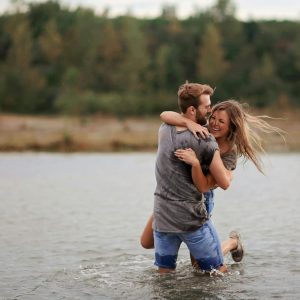 A young couple joyfully playing in the water against a natural backdrop, embodying love and happiness.